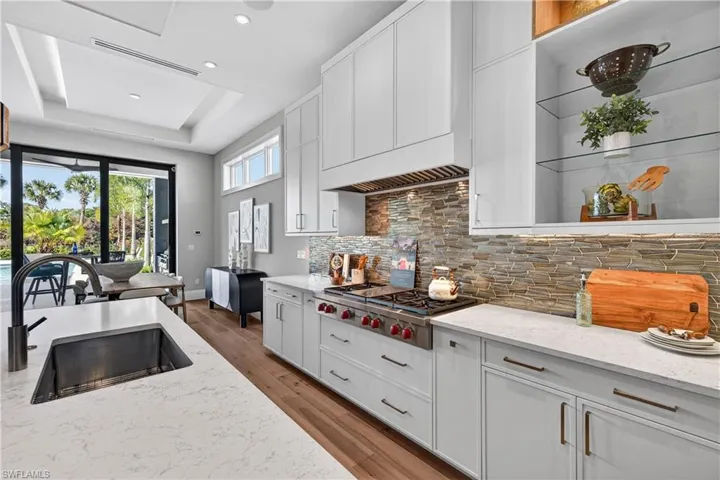 Kitchen with white cabinets, light stone counters, light wood-style flooring, stainless steel gas stovetop, and a raised ceiling