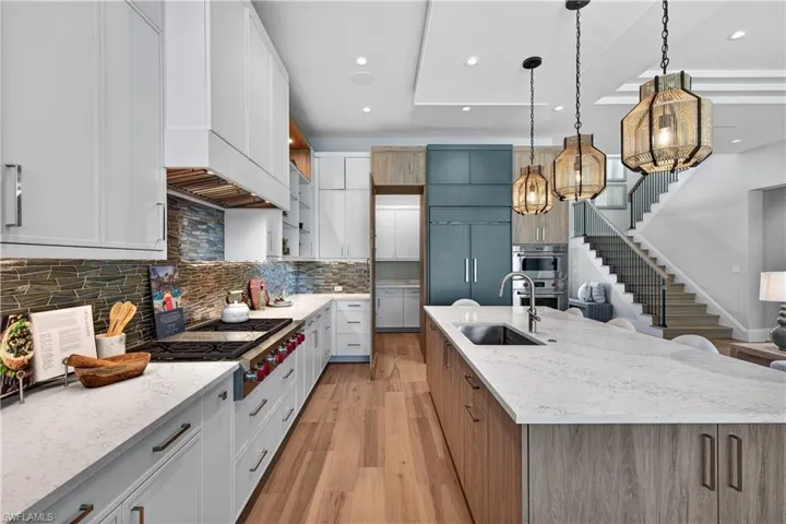 Dual tone kitchen with dual tone cabinets, light stone countertops, light wood-style flooring, pendant lighting, and modern cabinets