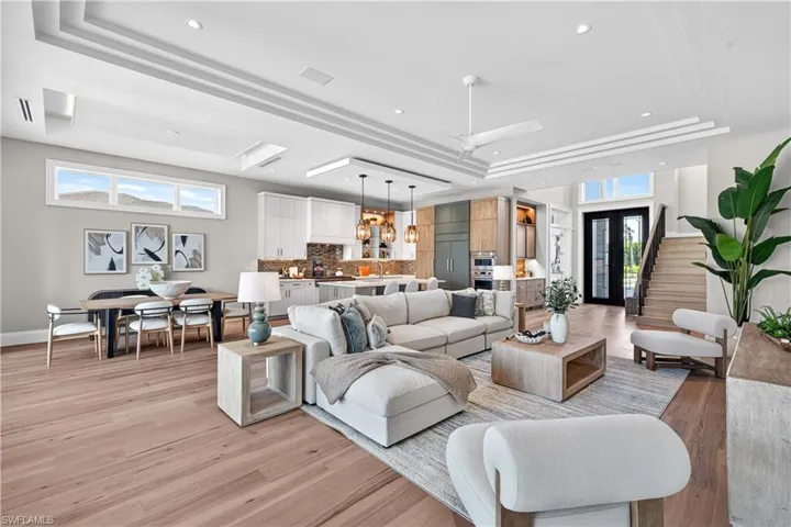 Living area with light wood-type flooring, plenty of natural light, a tray ceiling, a ceiling fan, and recessed lighting