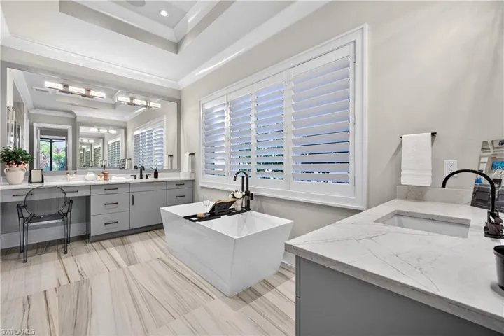 Full bathroom featuring two vanities, a soaking tub, a tray ceiling, ornamental molding, and recessed lighting