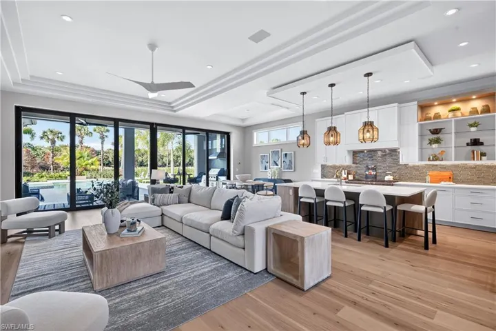 Living room featuring light wood finished floors, a tray ceiling, recessed lighting, and ceiling fan