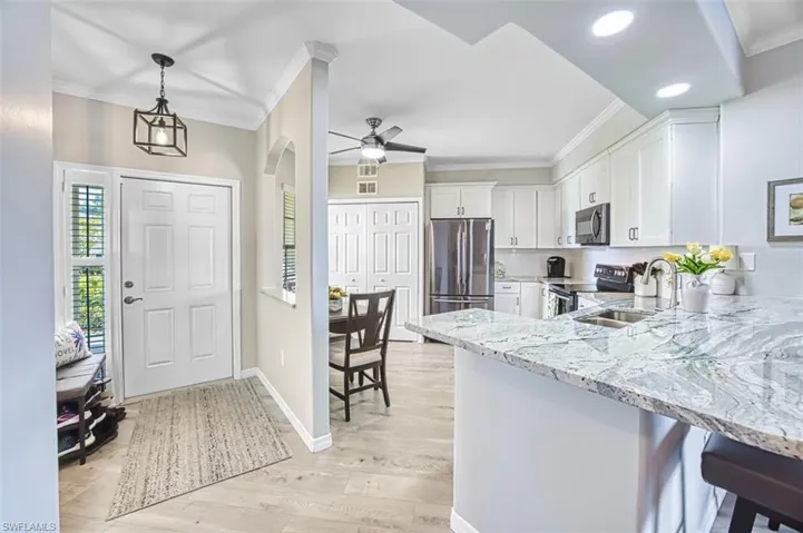 Kitchen featuring crown molding, light stone counters, a breakfast bar area, white cabinets, and pendant lighting