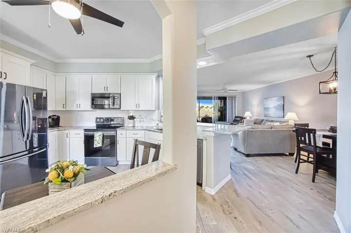 Kitchen with a ceiling fan, light stone counters, appliances with stainless steel finishes, open floor plan, and white cabinetry