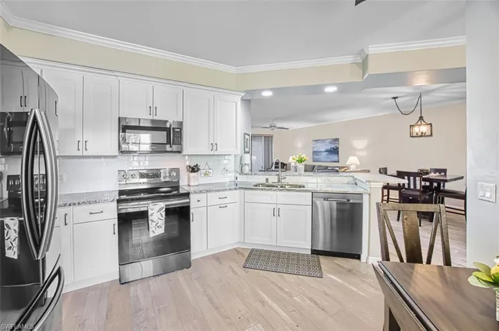 Kitchen featuring appliances with stainless steel finishes, a peninsula, white cabinets, light stone countertops, and backsplash