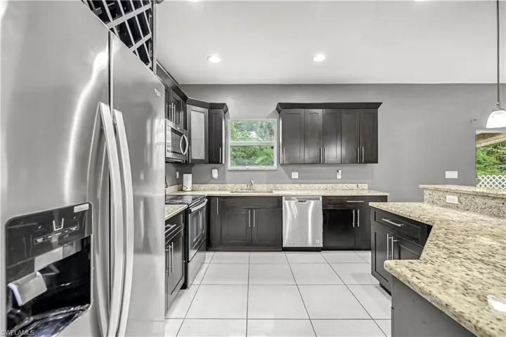 Kitchen featuring stainless steel appliances, light stone countertops, light tile patterned floors, decorative light fixtures, and recessed lighting