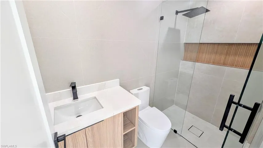 Bathroom featuring a modern wood-finish vanity with a quartz countertop, matte black hardware, a glass-enclosed shower, and wood-slat shower niche detailing