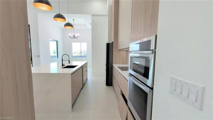 Kitchen featuring flat-panel wood-finish cabinetry, a large island with a quartz countertop, a dual stainless steel wall oven, and matte black pendant lighting