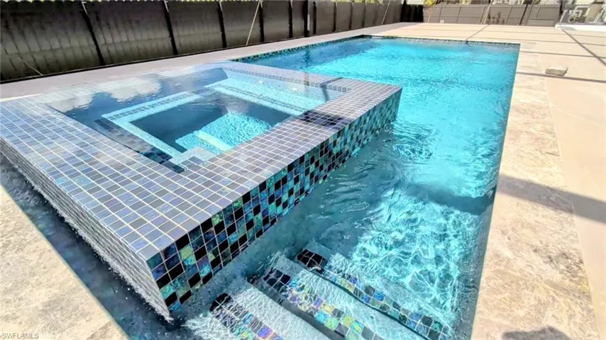 Inground swimming pool with a raised spillover spa, featuring iridescent glass tile accents and natural stone decking