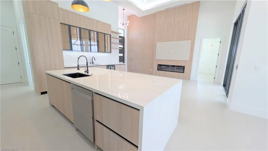 Modern kitchen featuring floor-to-ceiling wood-finish cabinetry, an oversized island with a solid-surface countertop, an integrated linear fireplace, and large-format porcelain tile flooring