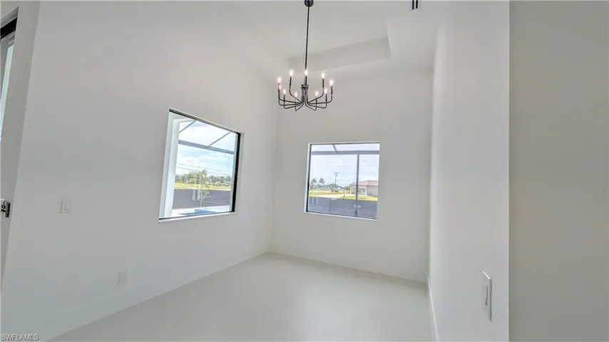 Interior space featuring high tray ceilings, large windows, tile flooring, and a modern multi-arm chandelier