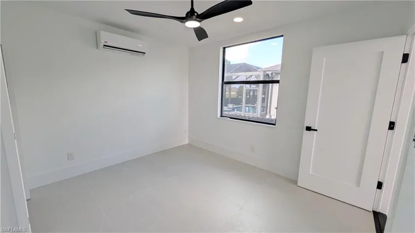 Interior space featuring large-format tile flooring, a wall-mounted ductless air conditioning unit, a matte black ceiling fan, recessed lighting, and a shaker-style interior door with matte black hardware
