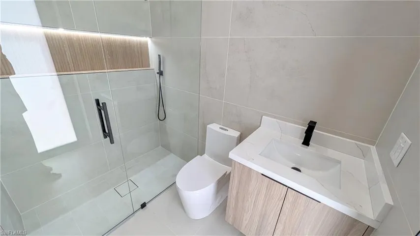Walk-in shower with floor-to-ceiling tile, wood-finish vanity with stone-top surface, undermount basin, and matte black hardware