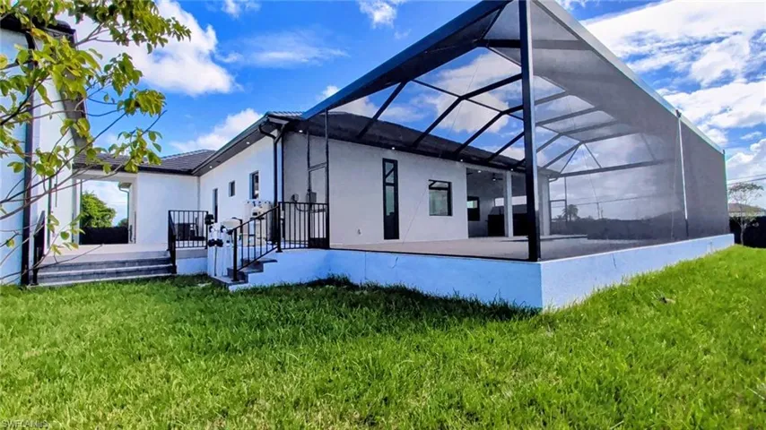 Exterior rear elevation featuring a covered screen-enclosed patio, concrete terrace, metal railings, and a concrete paver walkway