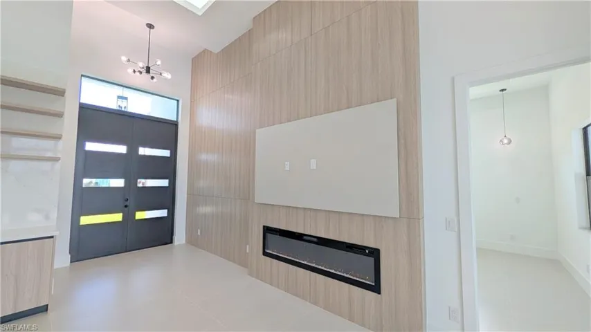 Double-entry door with transom window, full-height wood-finish accent wall, built-in linear electric fireplace, floating shelving, and modern multi-arm chandelier