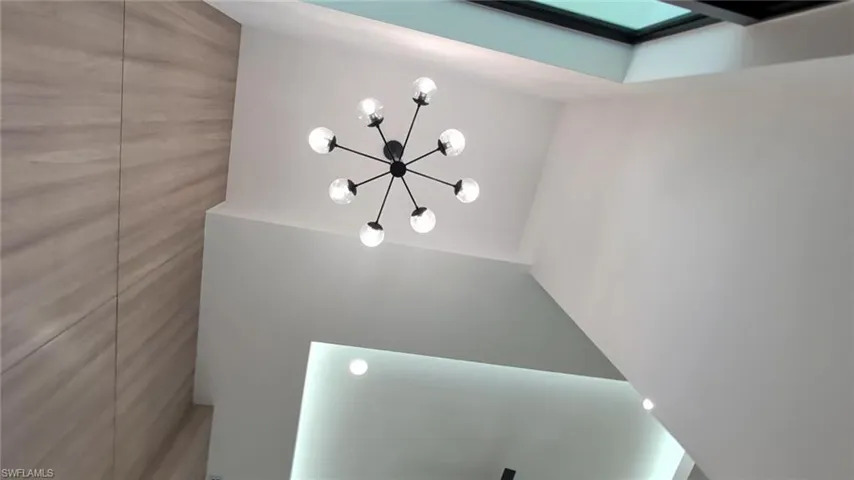 High-ceiling room featuring a wood-finish accent wall, multi-globe sputnik chandelier, recessed tray lighting, and a skylight