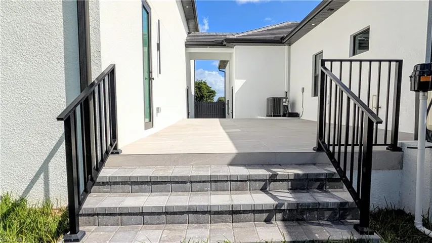 Exterior patio area featuring light-toned tile flooring, concrete paver steps, and matte black metal railings