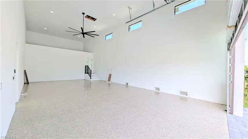 Spacious garage featuring high ceilings, epoxy-finish flooring, recessed lighting, a large ceiling fan, and clerestory windows