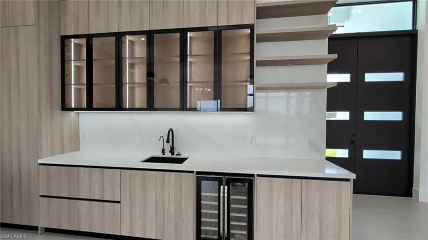 Wood-finish cabinetry, stone-surfaced countertop with integrated sink, black metal hardware, glass-front upper cabinets, and built-in under-counter beverage refrigeration