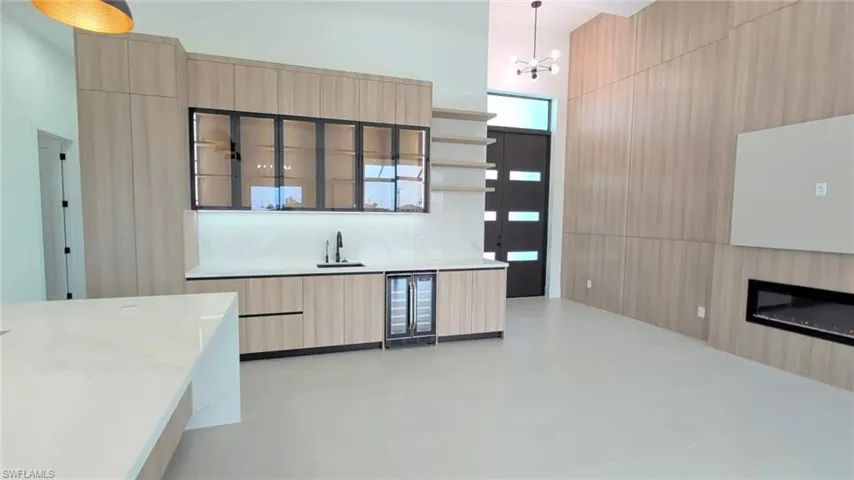 Full-height wood-finish cabinetry, floor-to-ceiling accent wall, built-in linear fireplace, quartz countertop wet bar with integrated beverage cooler, and multi-panel glass entry door
