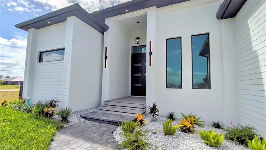 Contemporary exterior featuring white smooth-finish siding, a dark-toned modern entry door with glass inserts, recessed lighting, and integrated vertical wall sconces