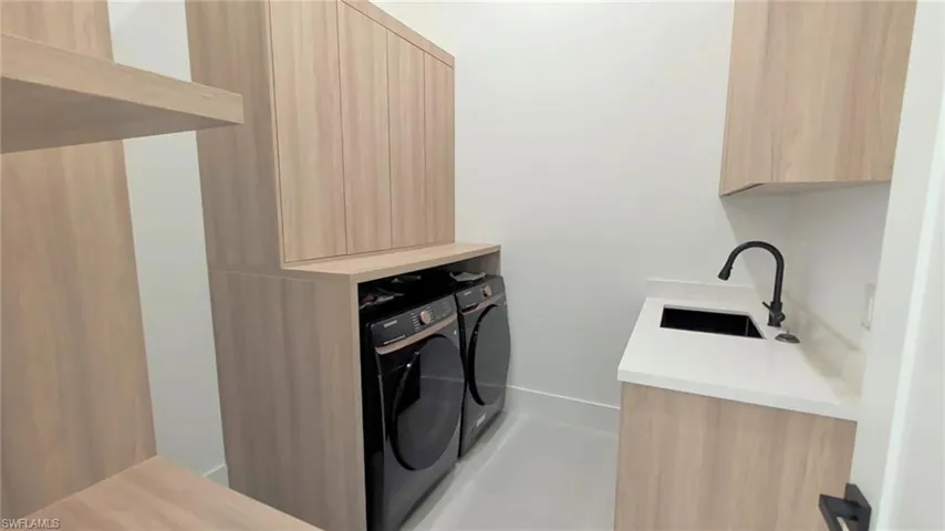Laundry area featuring light wood-finish built-in cabinetry, white countertops, a drop-in sink with a matte black faucet, and overhead storage