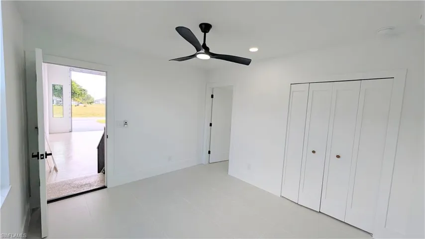 Neutral-toned interior featuring large-format tile flooring, a matte black three-blade ceiling fan, recessed lighting, and a closet with bifold doors