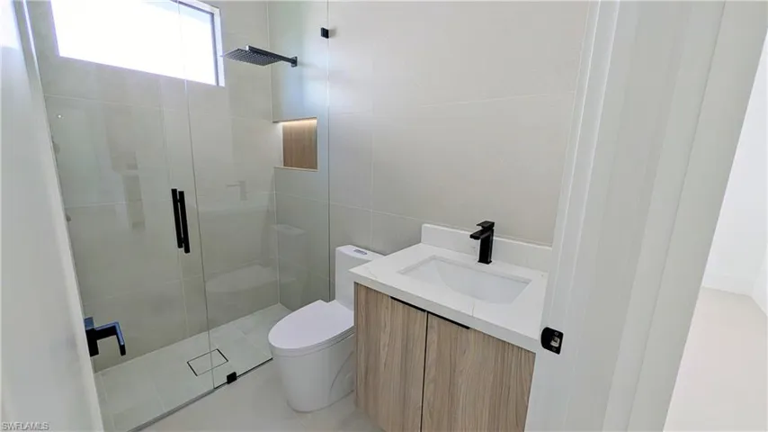 Bathroom featuring a floating vanity with wood-finish cabinetry, a white stone-surface countertop, a glass-enclosed shower with a rainfall showerhead, and matte black fixtures