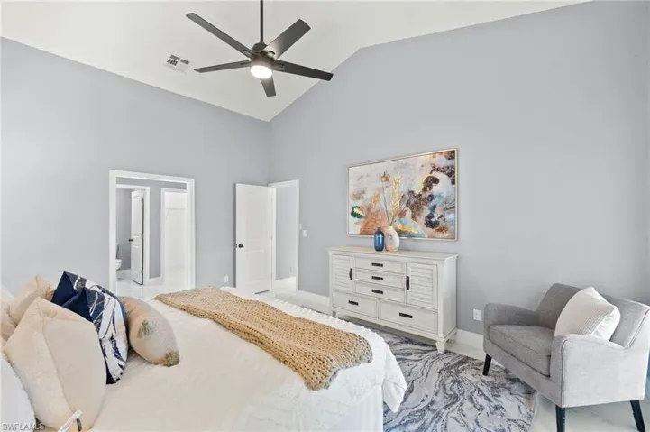 Bedroom with high vaulted ceiling, baseboards, ceiling fan, and connected bathroom