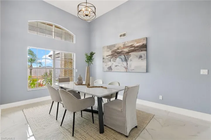 Dining room featuring light marble finish flooring, baseboards, a chandelier, and a towering ceiling