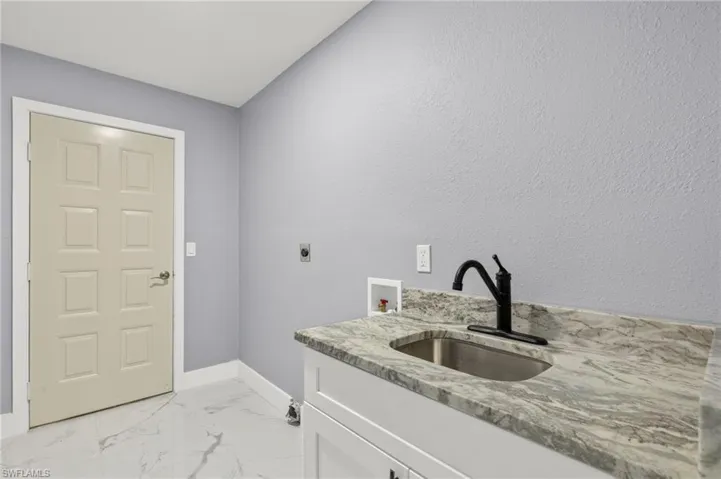 Washroom featuring hookup for an electric dryer, cabinet space, washer hookup, baseboards, and light marble finish floors