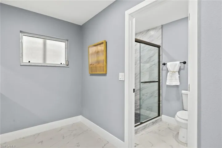 Full bathroom with marble finish floors, toilet, a marble finish shower, and baseboards