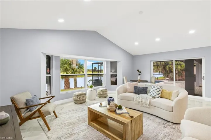 Living room featuring marble look tiles, vaulted ceiling, recessed lighting, and a water view