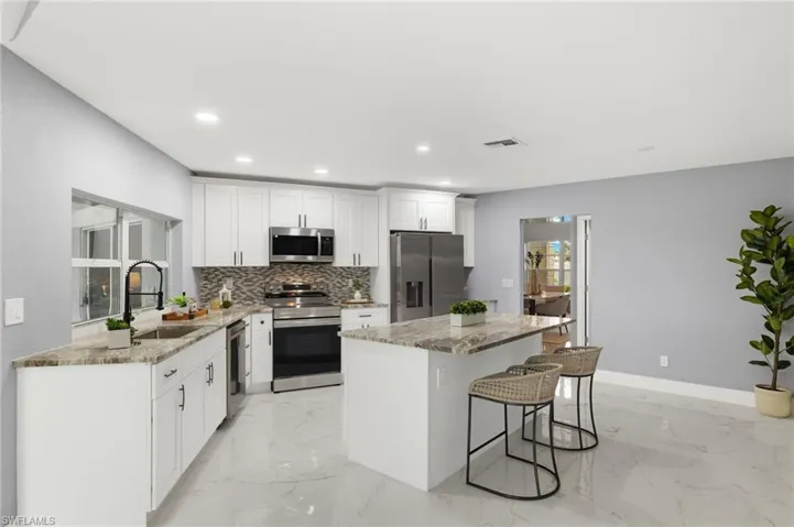 Kitchen featuring appliances with stainless steel finishes, a sink, a kitchen island, backsplash, and light marble finish floors