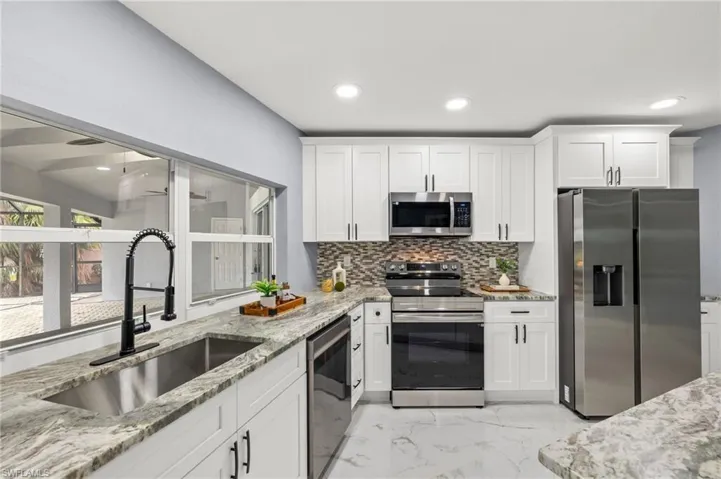 Kitchen featuring appliances with stainless steel finishes, a sink, light marble finish floors, tasteful backsplash, and white cabinets