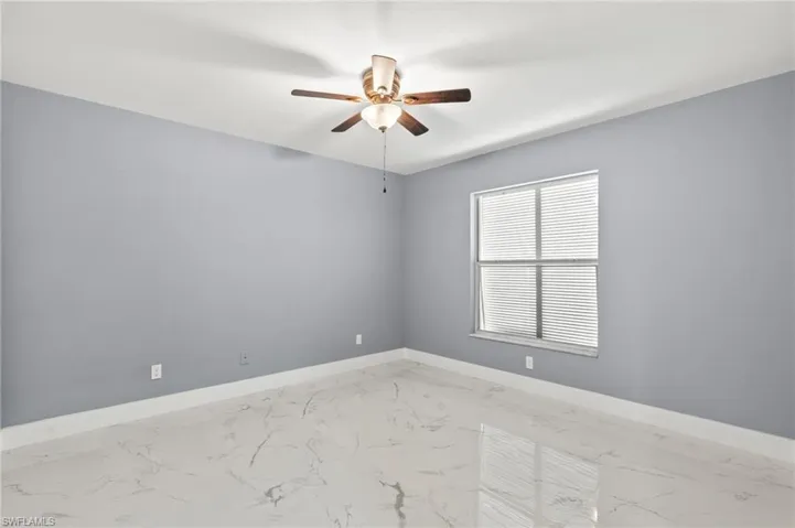 Empty room featuring light marble finish flooring, ceiling fan, and baseboards