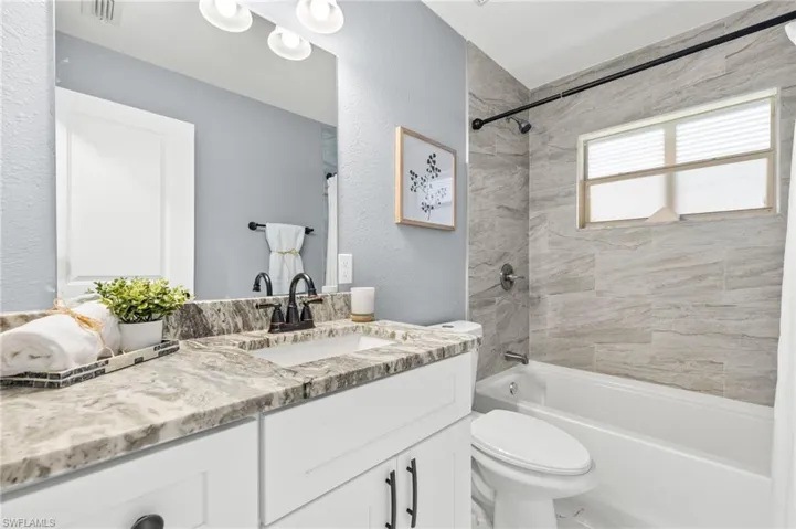 Bathroom with toilet, shower / bathtub combination, vanity, and a textured wall