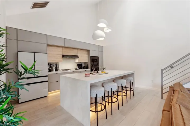Kitchen with an island with sink, high vaulted ceiling, a kitchen breakfast bar, and light tile flooring
