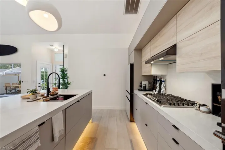 Kitchen with light tile flooring, stainless steel gas stovetop, wall  exhaust hood, unique refrigerator, and sink
