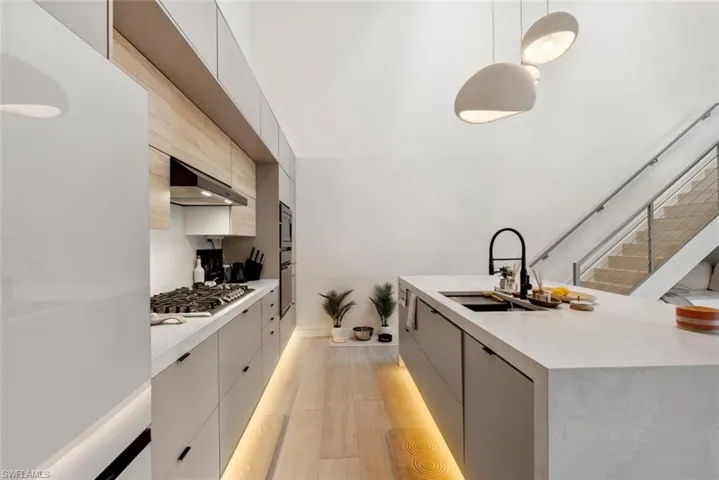 Kitchen featuring stainless steel appliances, light tile flooring, wall exhaust hood, decorative light fixtures, and sink