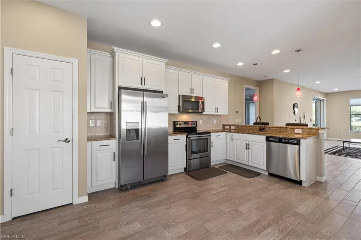 Kitchen with white cabinetry, stainless steel appliances, kitchen peninsula, decorative light fixtures, and light wood-type flooring
