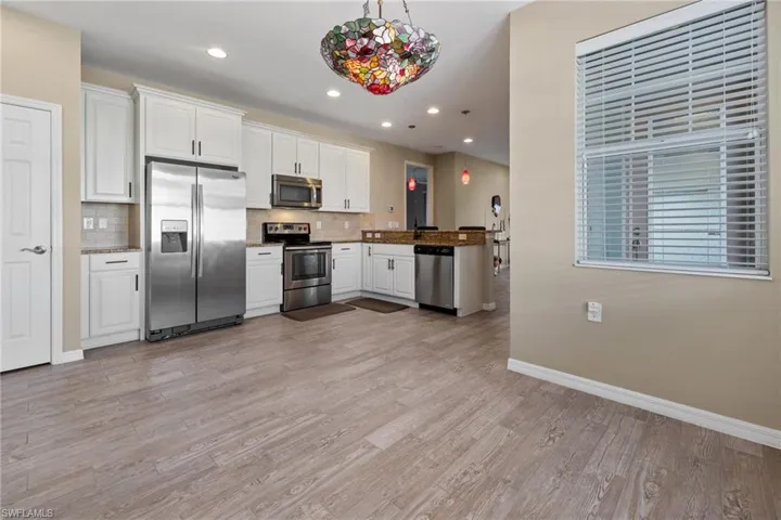 Kitchen with white cabinetry, hanging light fixtures, tasteful backsplash, appliances with stainless steel finishes, and light wood-type flooring