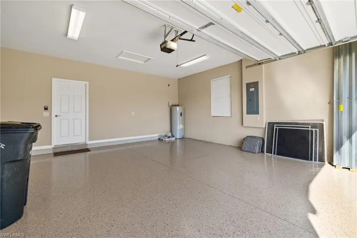 Garage featuring electric water heater, electric panel, and a garage door opener
