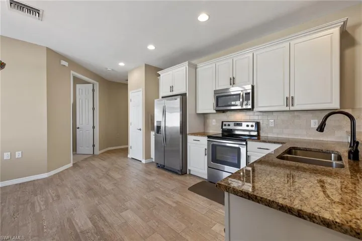 Kitchen with backsplash, dark stone counters, white cabinets, sink, and stainless steel appliances