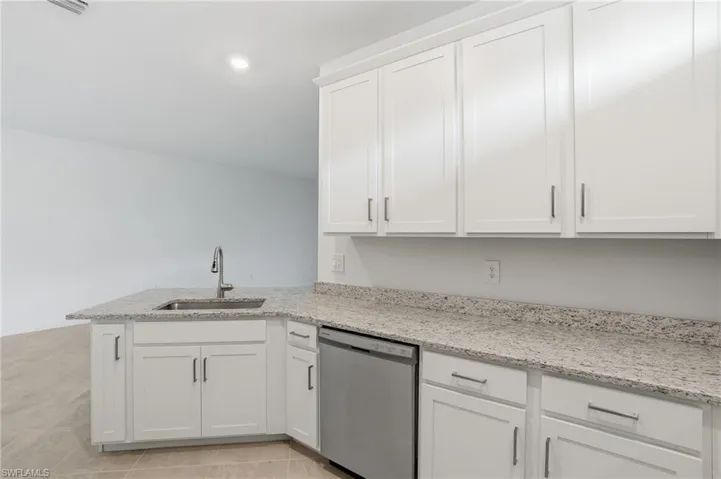 Kitchen with white cabinets, dishwasher, light stone counters, a peninsula, and light tile patterned flooring