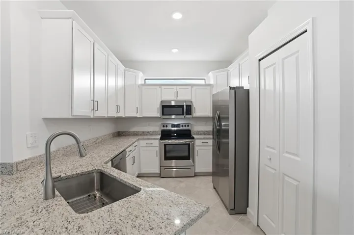 Kitchen featuring appliances with stainless steel finishes, white cabinetry, light stone countertops, and recessed lighting