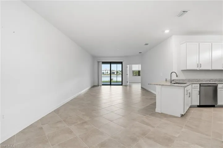 Kitchen with white cabinets, dishwasher, light stone counters, open floor plan, and a peninsula