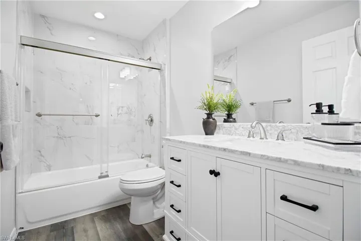 Full bath featuring bath / shower combo with glass door, toilet, recessed lighting, wood finished floors, and vanity