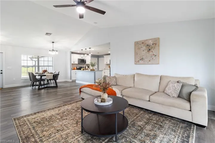 Living area featuring lofted ceiling, visible vents, dark wood-style flooring, and ceiling fan with notable chandelier