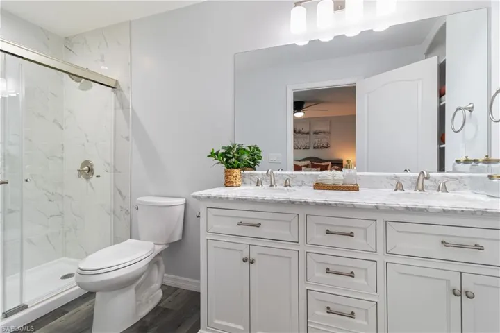 Full bath with a marble finish shower, toilet, ceiling fan, and a sink