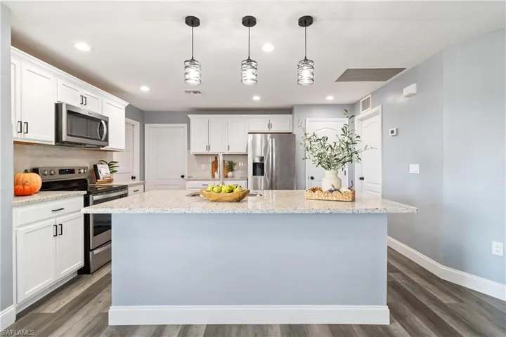 Kitchen featuring an island with sink, white cabinetry, backsplash, baseboards, and appliances with stainless steel finishes